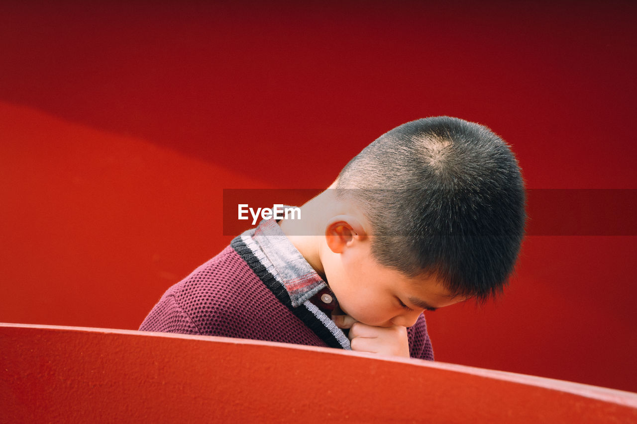 Boy looking away against red background