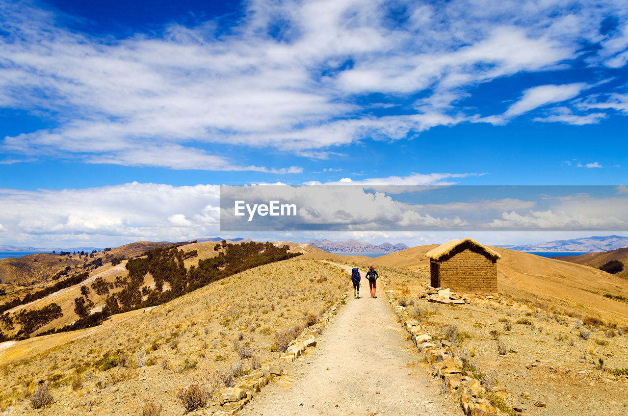 Rear view of hikers walking on dirt road at isla del sol against sky