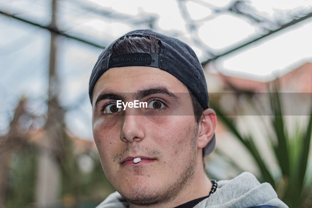 CLOSE-UP PORTRAIT OF YOUNG MAN WEARING HAT