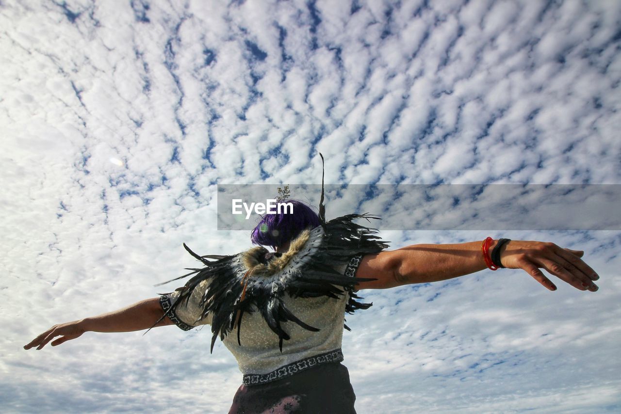 Low angle view of woman standing against cloudy sky