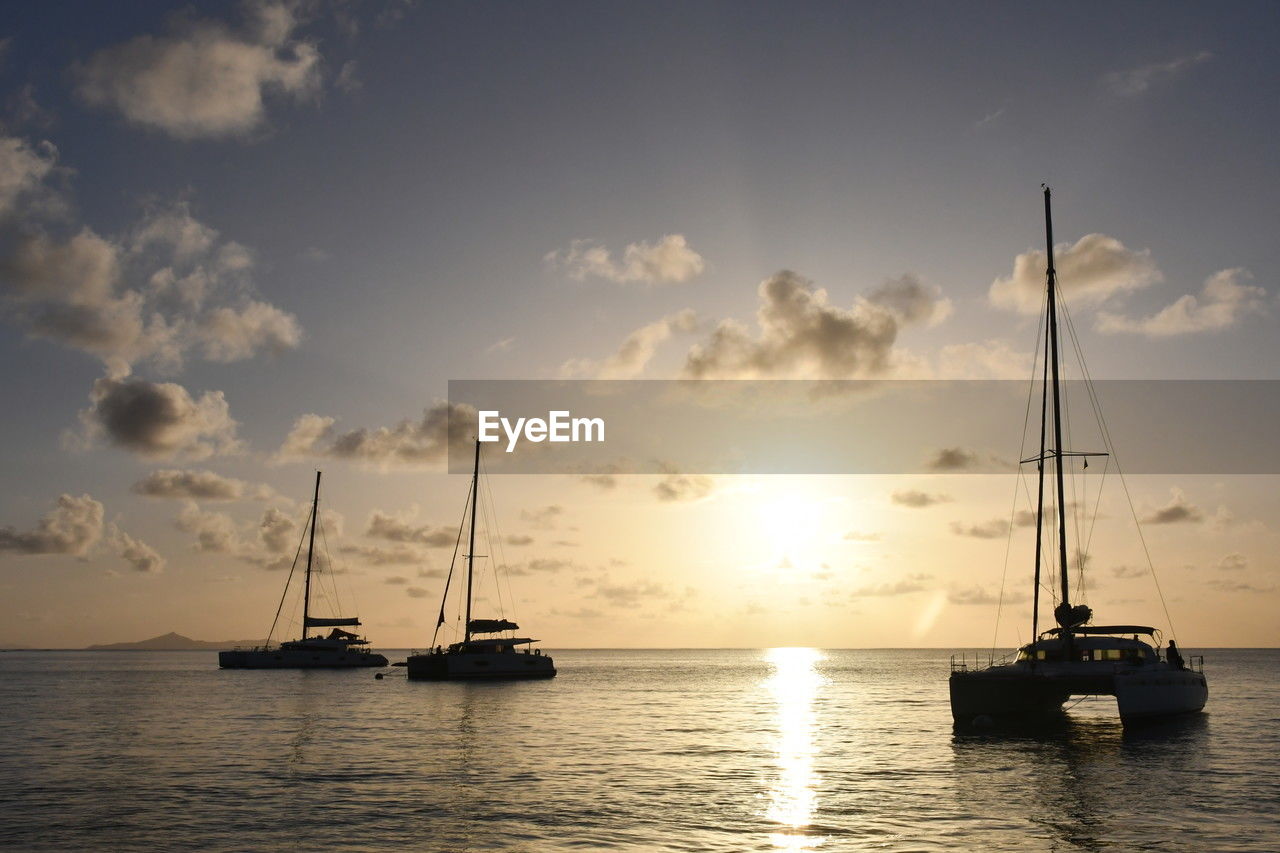 Scenic view of sea and catamaran against sky during sunset