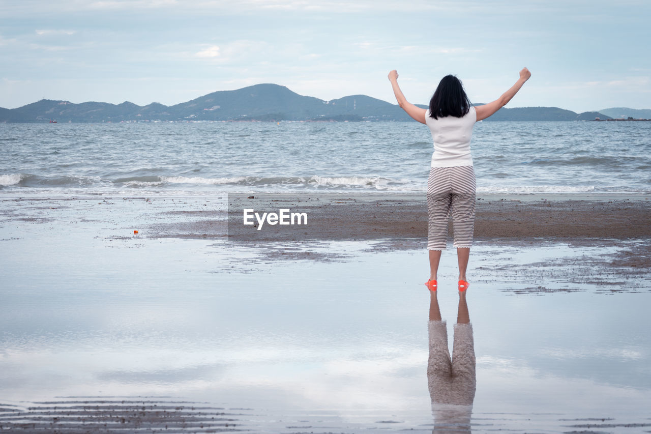 REAR VIEW OF WOMAN STANDING AT BEACH