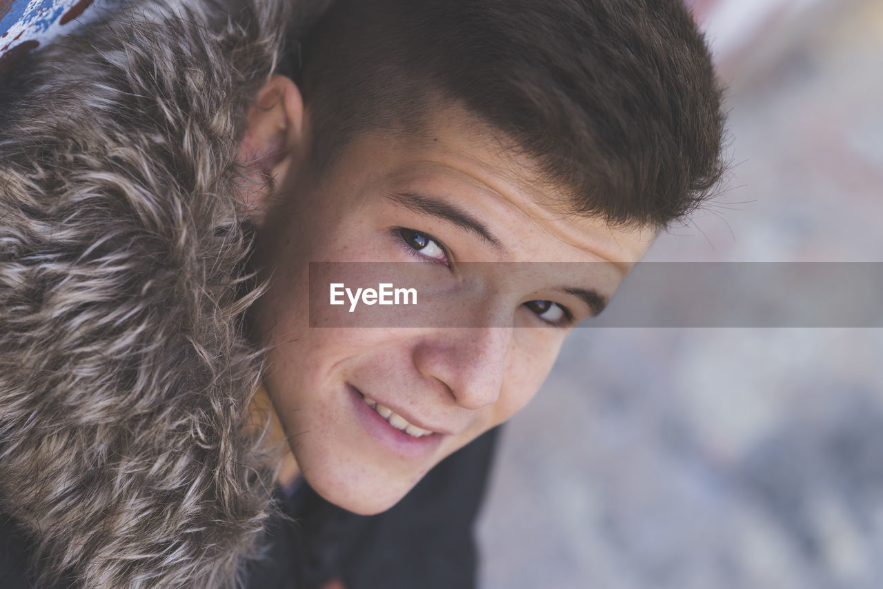 Close-up portrait of smiling teenage boy wearing fur coat during winter