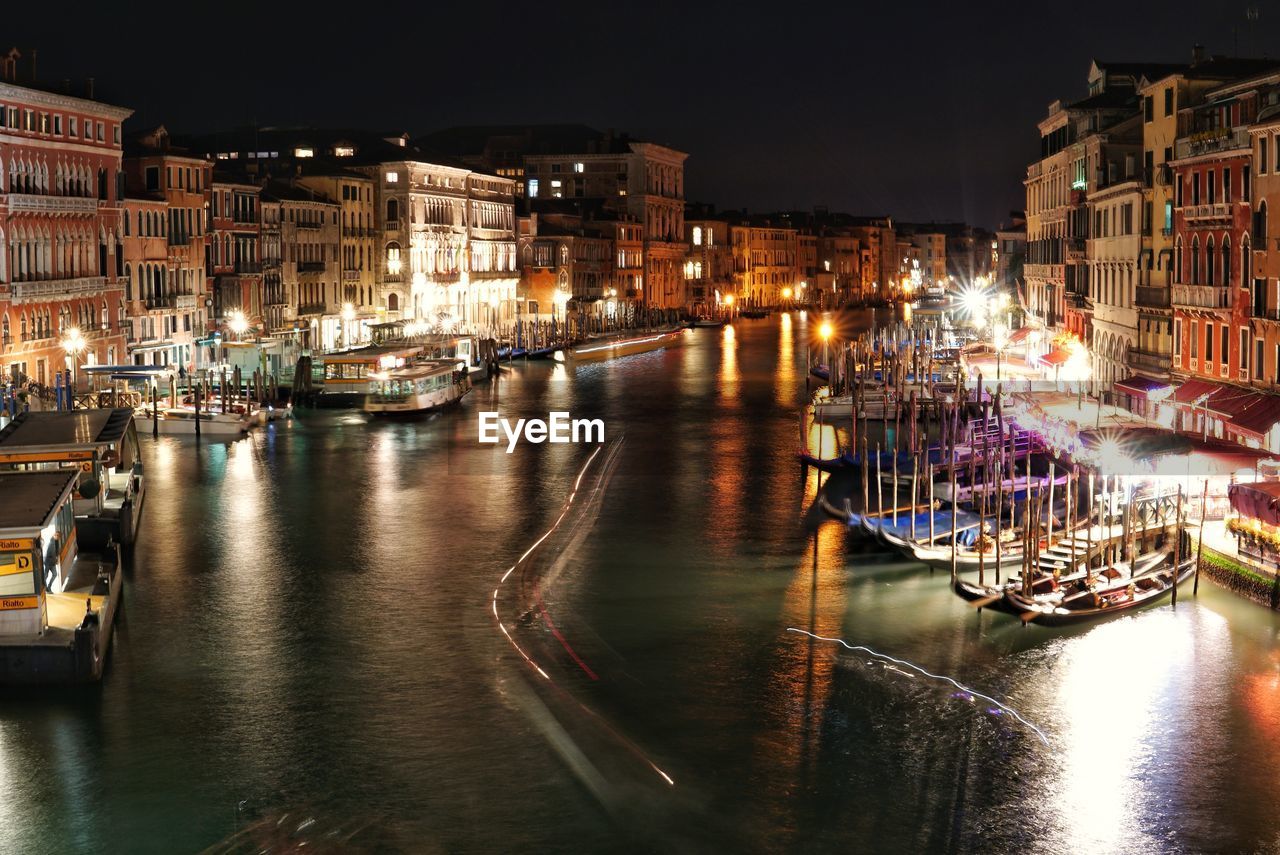 SAILBOATS MOORED ON ILLUMINATED CITY BUILDINGS AT NIGHT