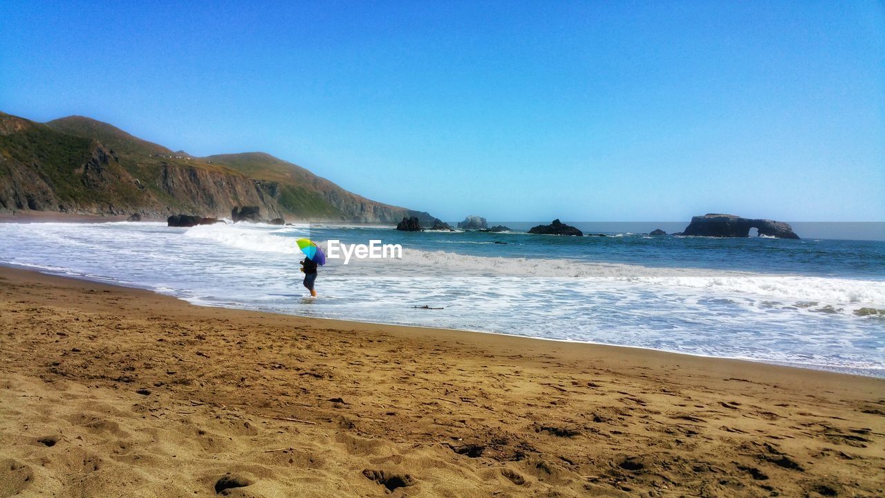 Man at beach against clear blue sky