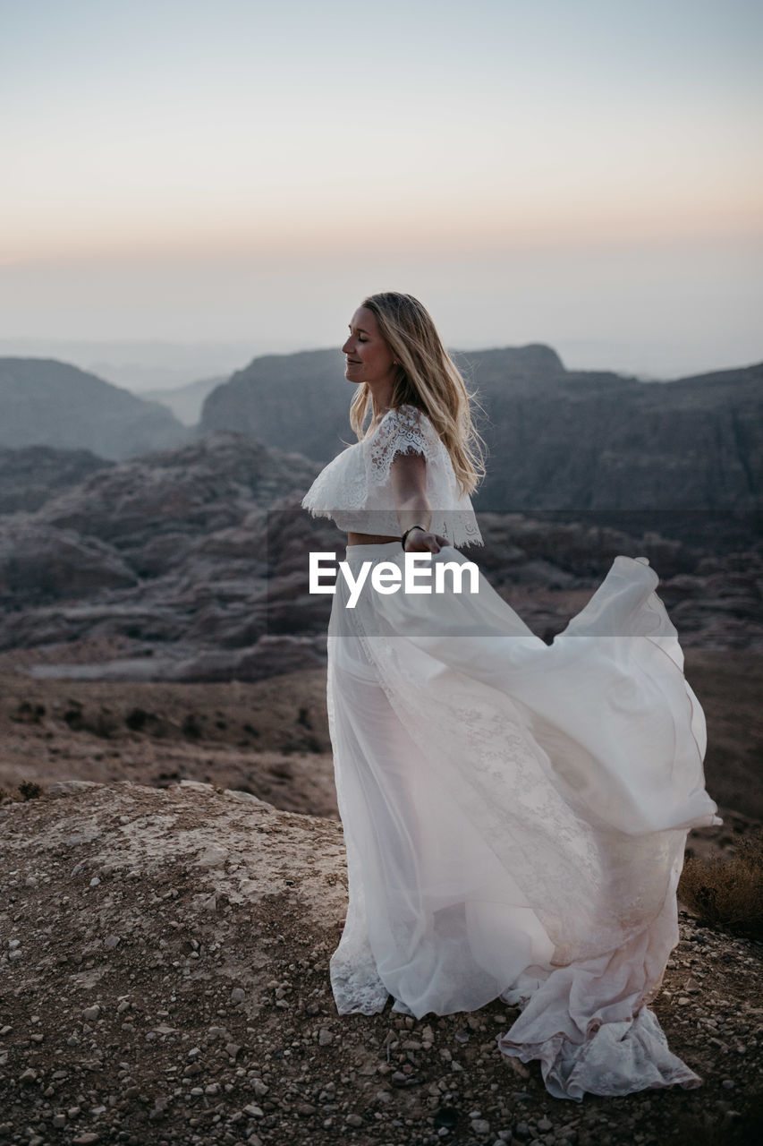 Woman in dress standing on landscape against sky