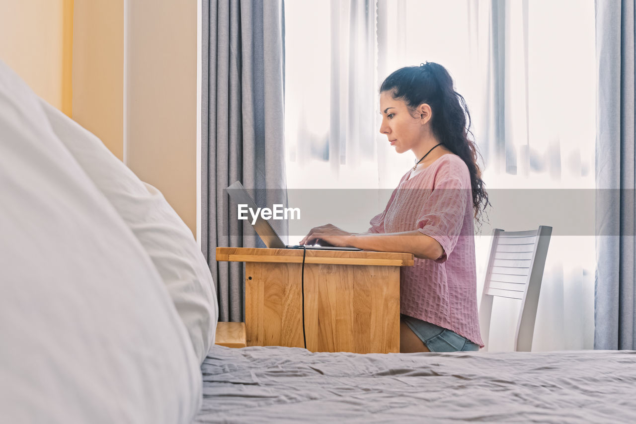 Portrait of serious beautiful young woman working  at home. in foreground is a bed with pillows