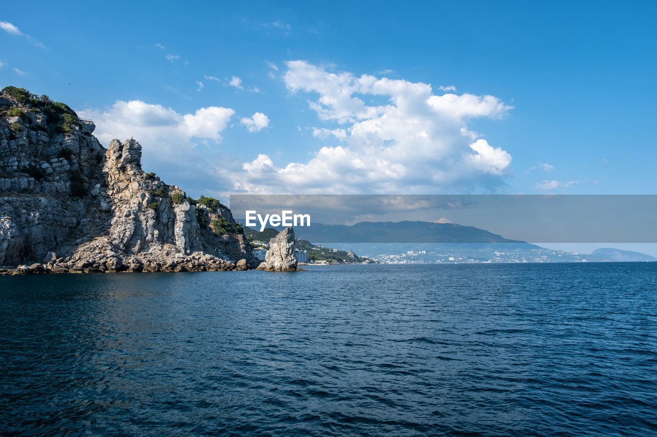 Scenic view of sea by mountain against sky