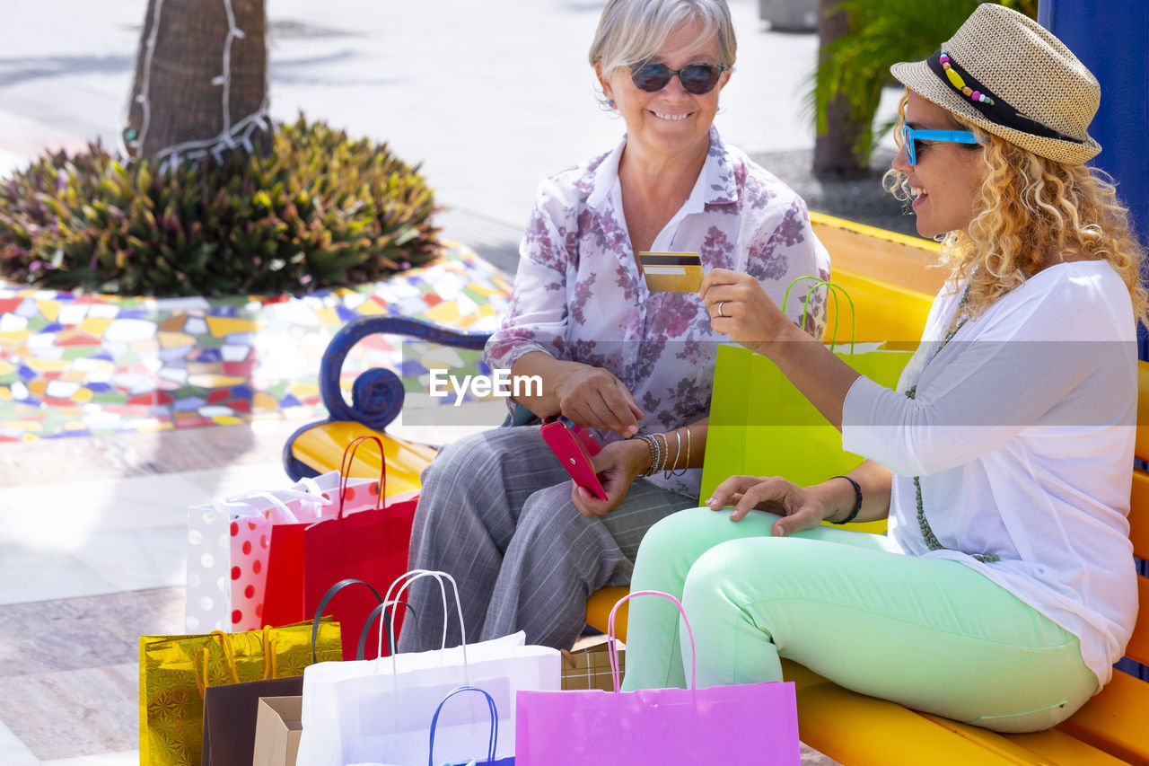 Daughter holding credit card while sitting with mother on bench