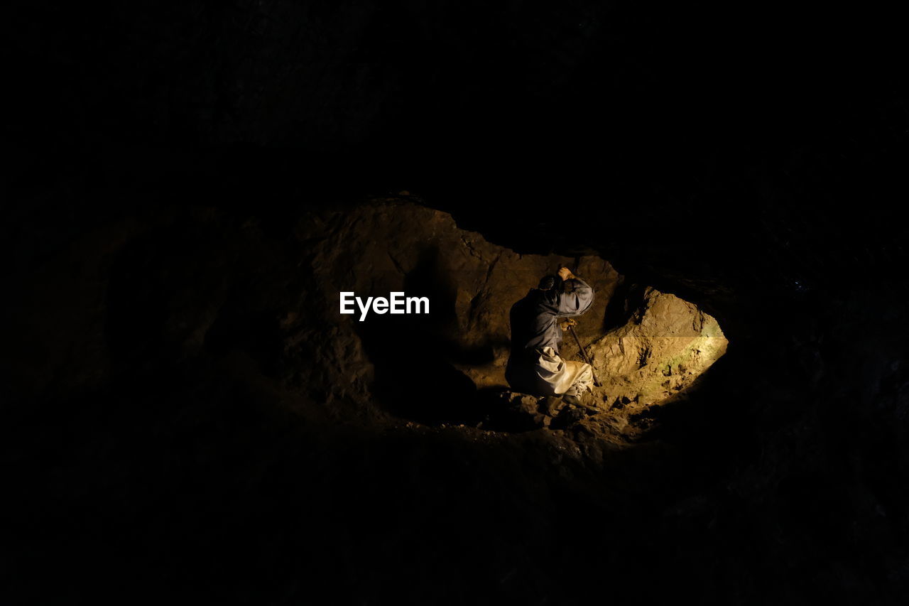 Side view of manual worker breaking rock in dark cave