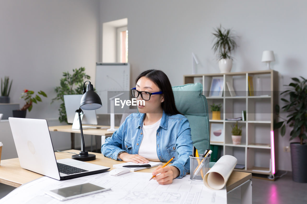 young woman using laptop while sitting at desk in office
