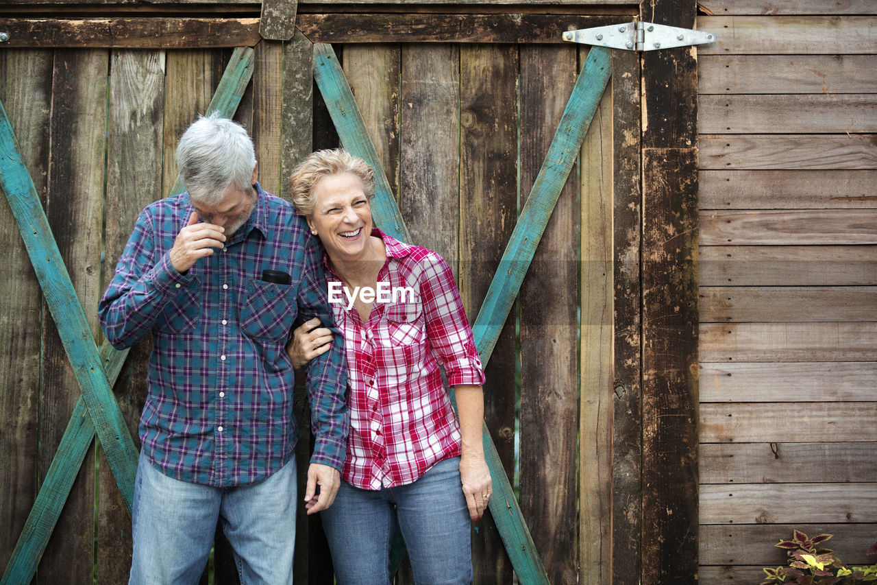 Happy senior couple standing against log cabin in forest