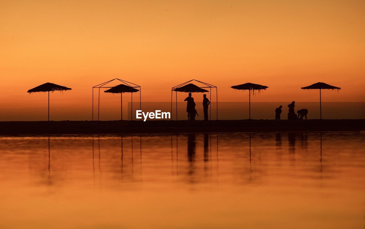 Silhouette people on beach against sky during sunset