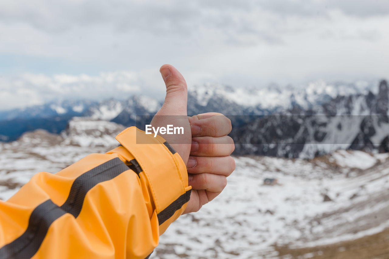 Close-up of hand showing thumbs up against sky