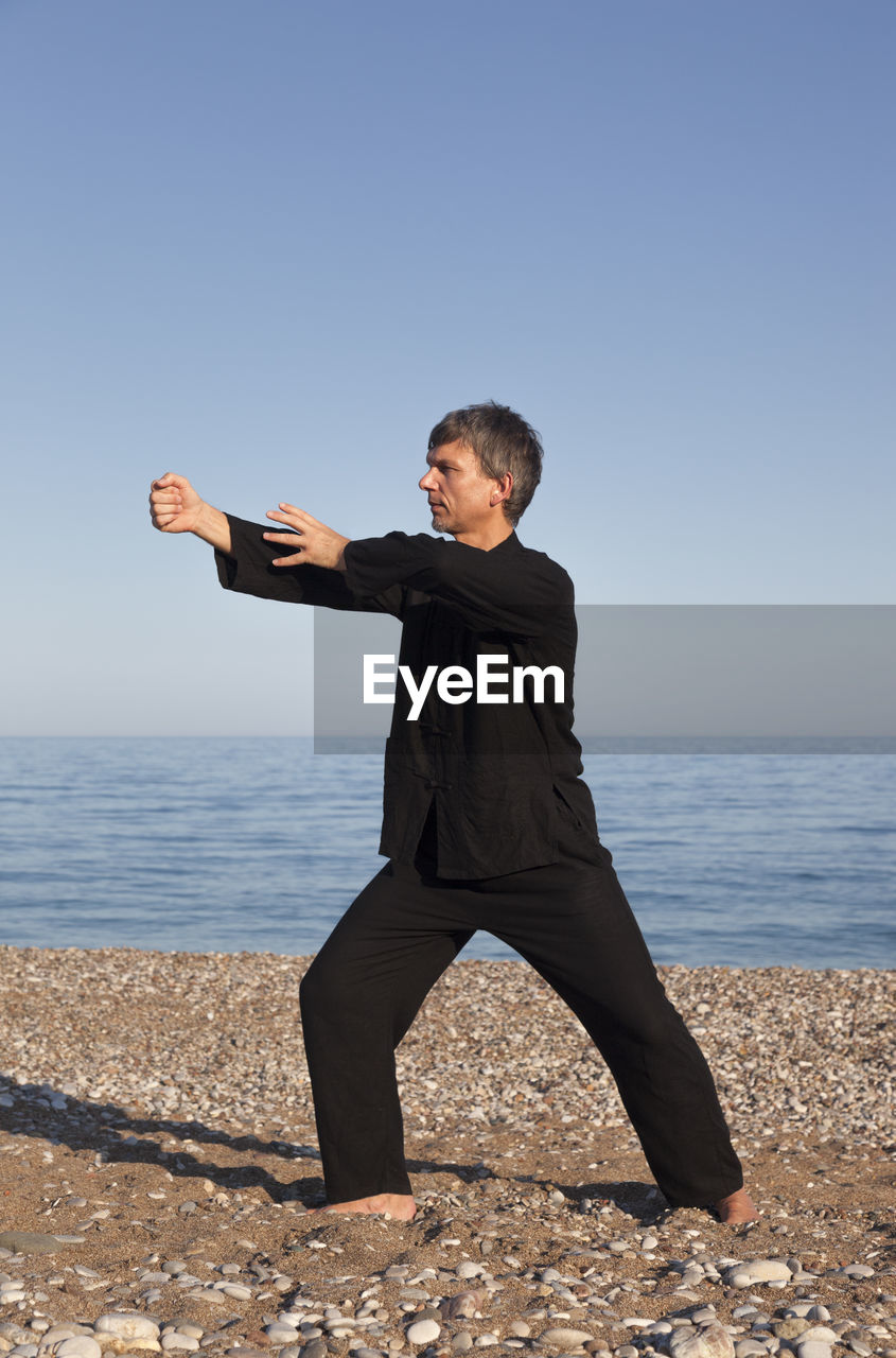 Mature man practicing martial arts at beach against sky