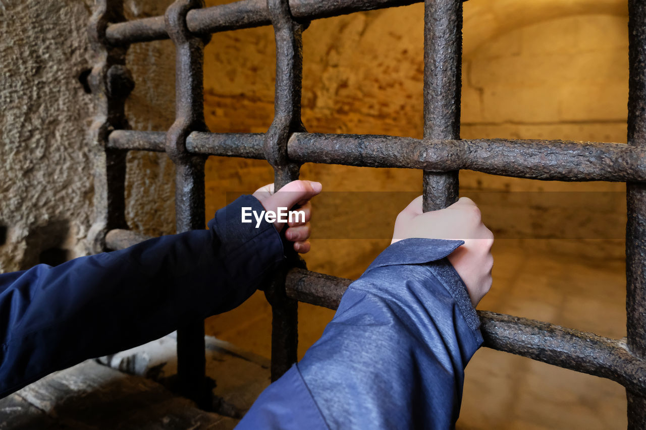 Hands holding metal bars in prison window