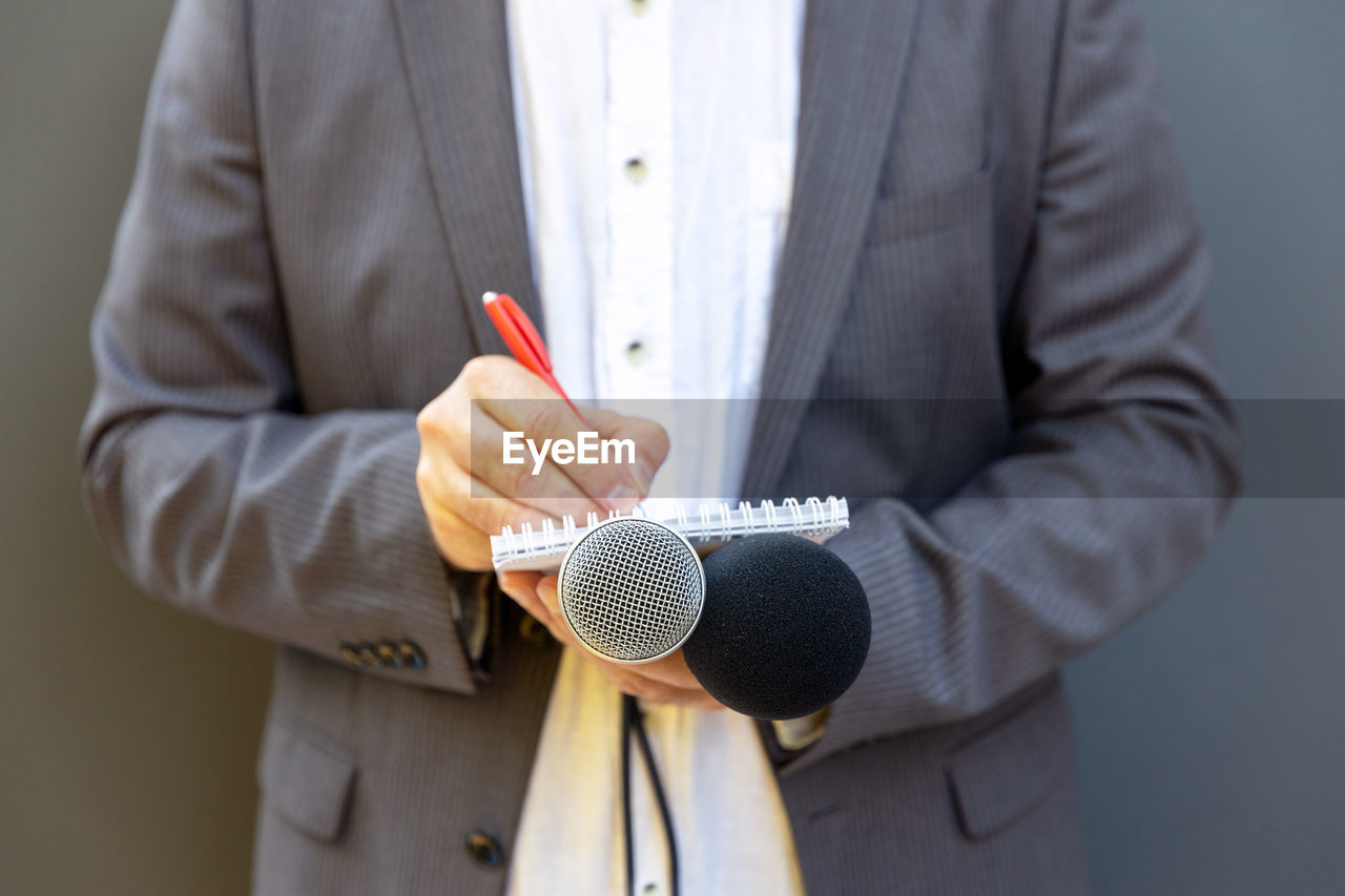 Male journalist at press conference or media event, writing notes, holding microphone