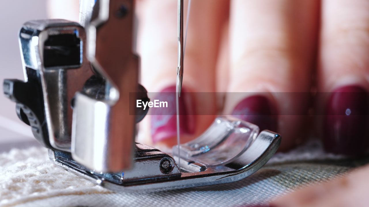 Cropped hand of tailor using sewing machine while stitching textile