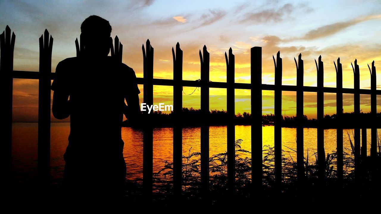 Rear view of silhouette man looking at lake during sunset