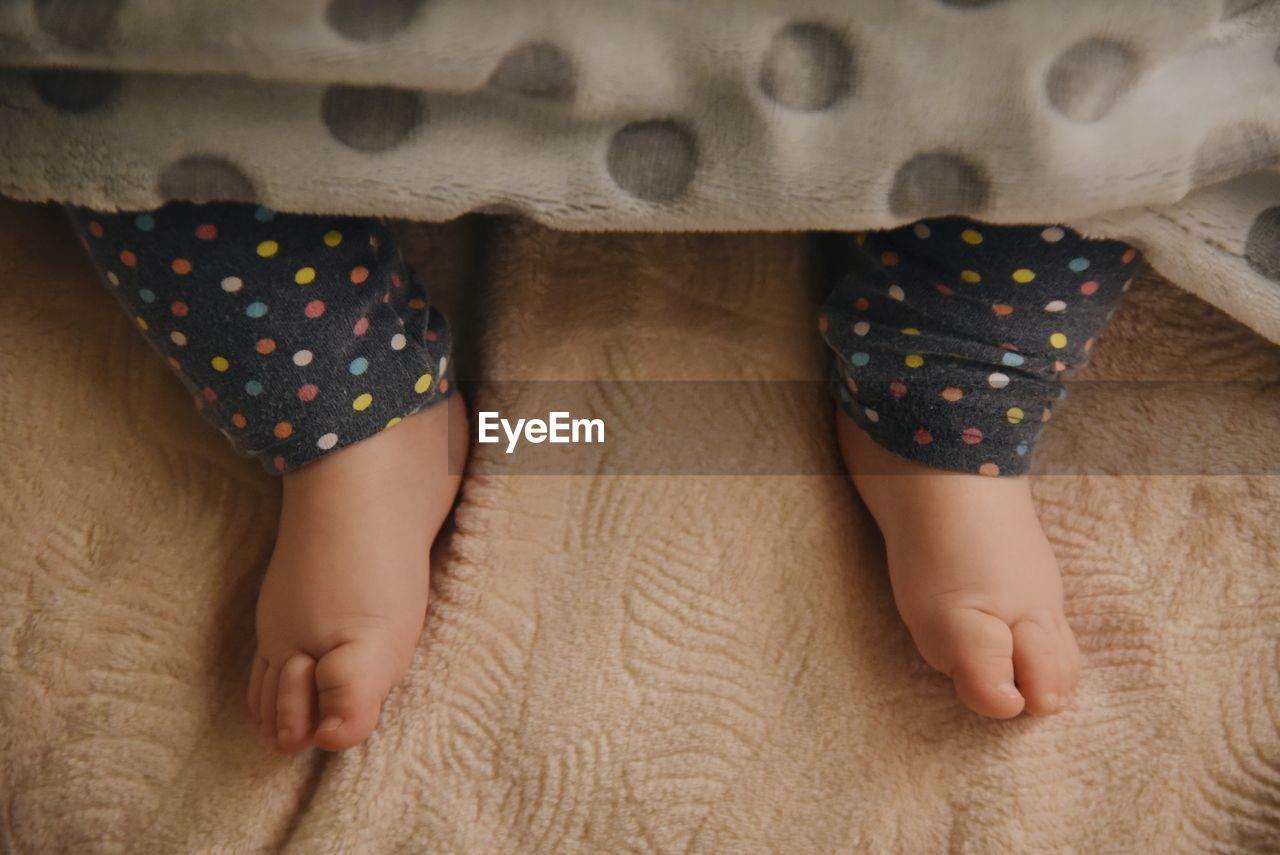 Low section of baby feet lying on bed under blanket 
