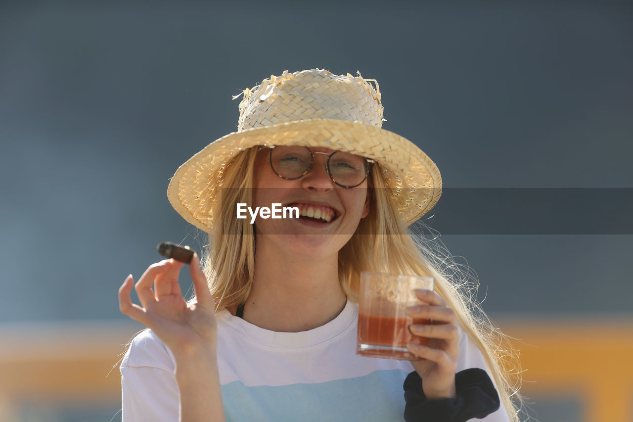 PORTRAIT OF SMILING WOMAN HOLDING HAT