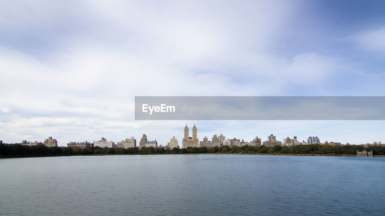 City at waterfront against cloudy sky