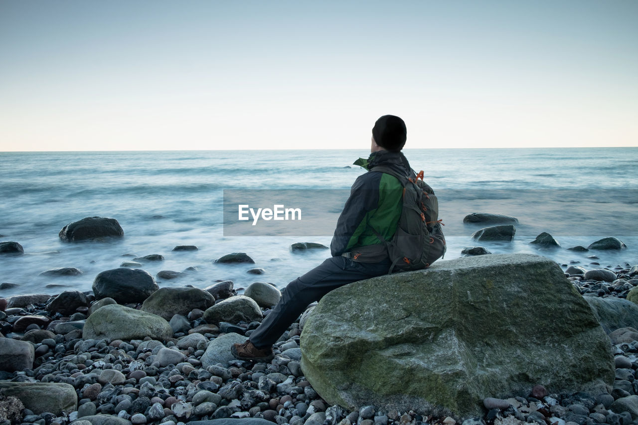 Hiker is looking out to sea stack. evening at calm blue sea, stony beach.