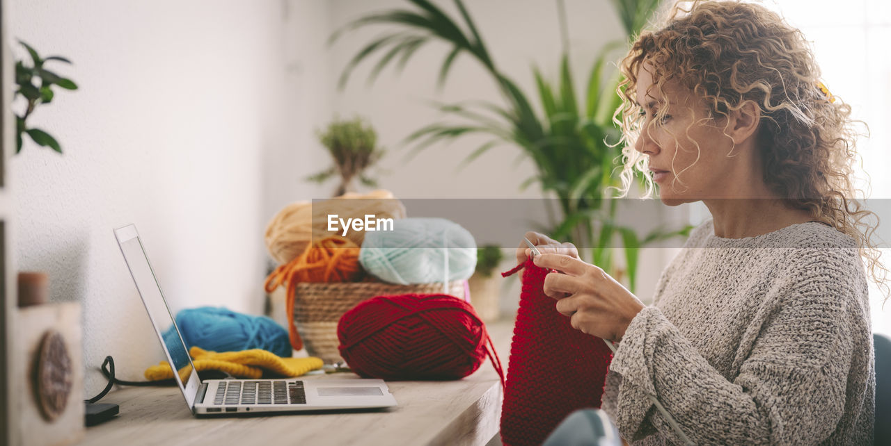 Woman knitting while looking at laptop