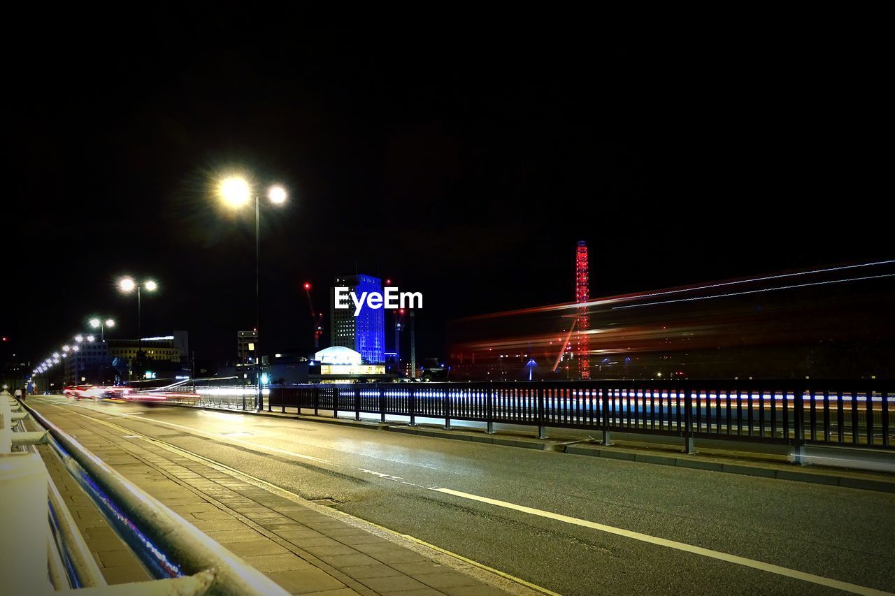 LIGHT TRAILS ON ROAD IN CITY AT NIGHT