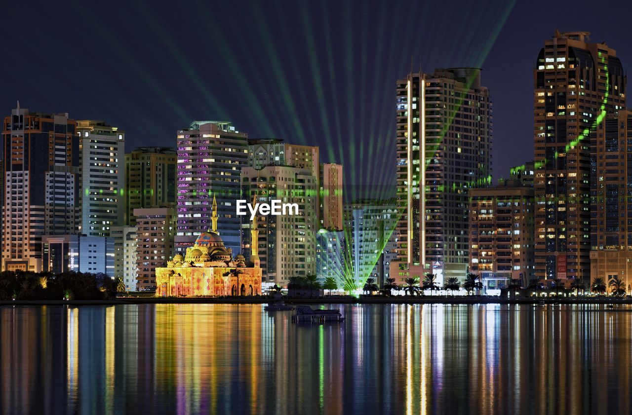 Illuminated buildings by river against sky at night