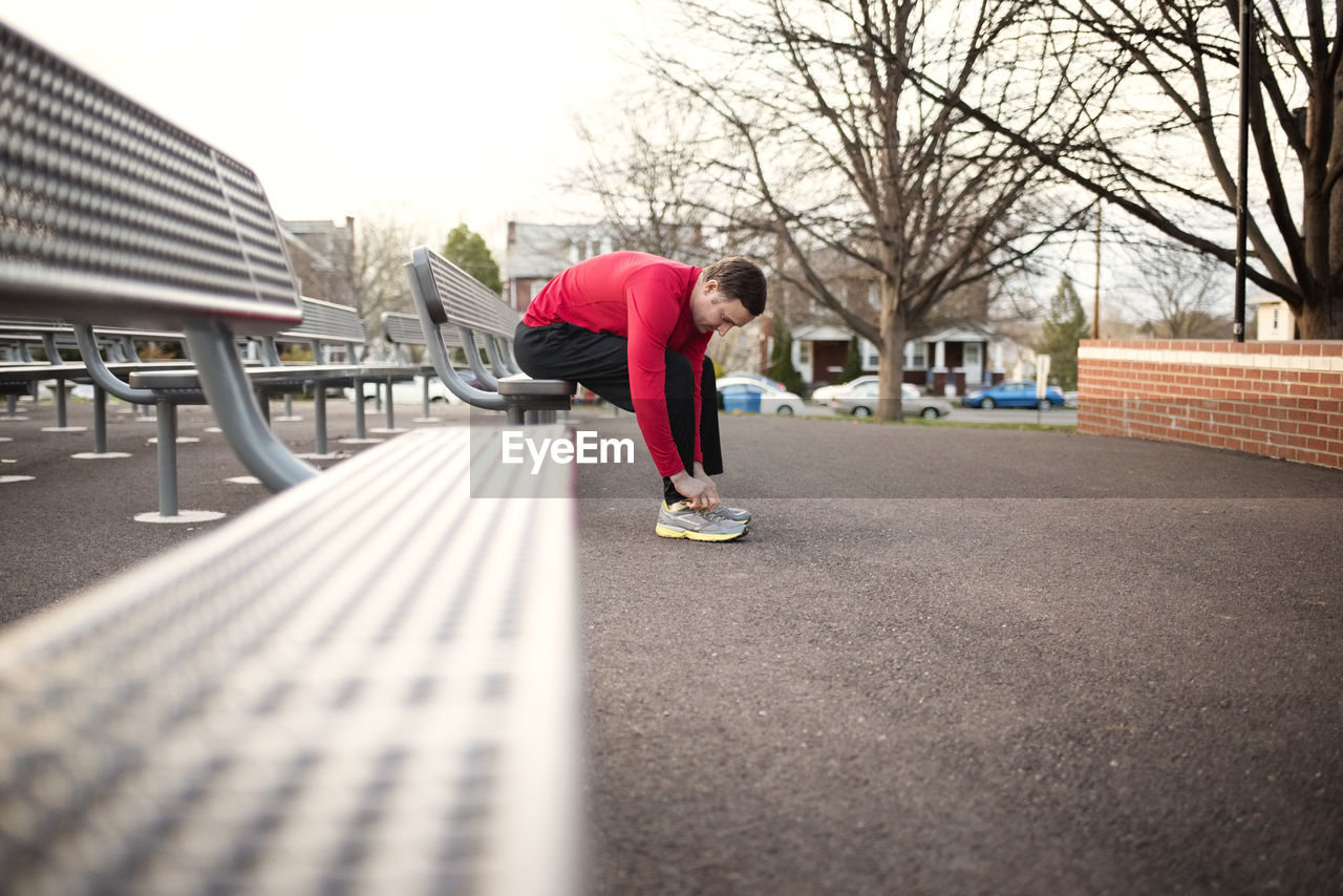 Sporty man wearing shoes while sitting on bench at park