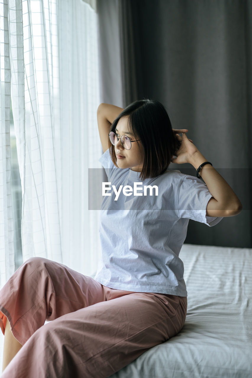 YOUNG WOMAN SITTING ON BED AT HOME