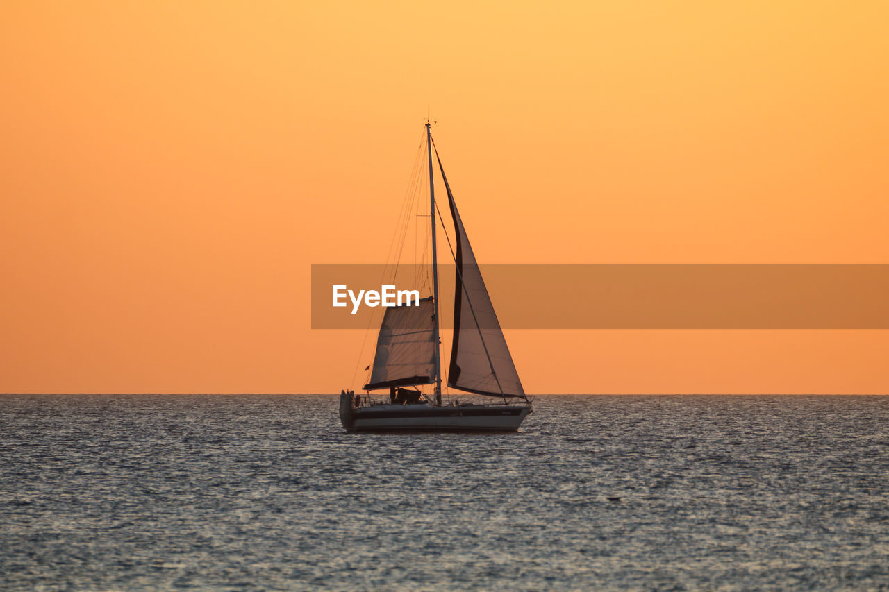 Sailboat sailing on sea against orange sky