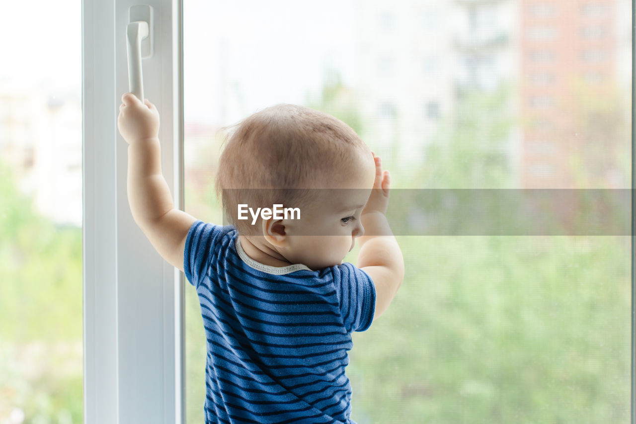 Rear view of boy standing by window at home