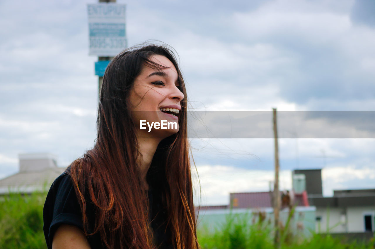 Portrait of smiling young woman in city against sky
