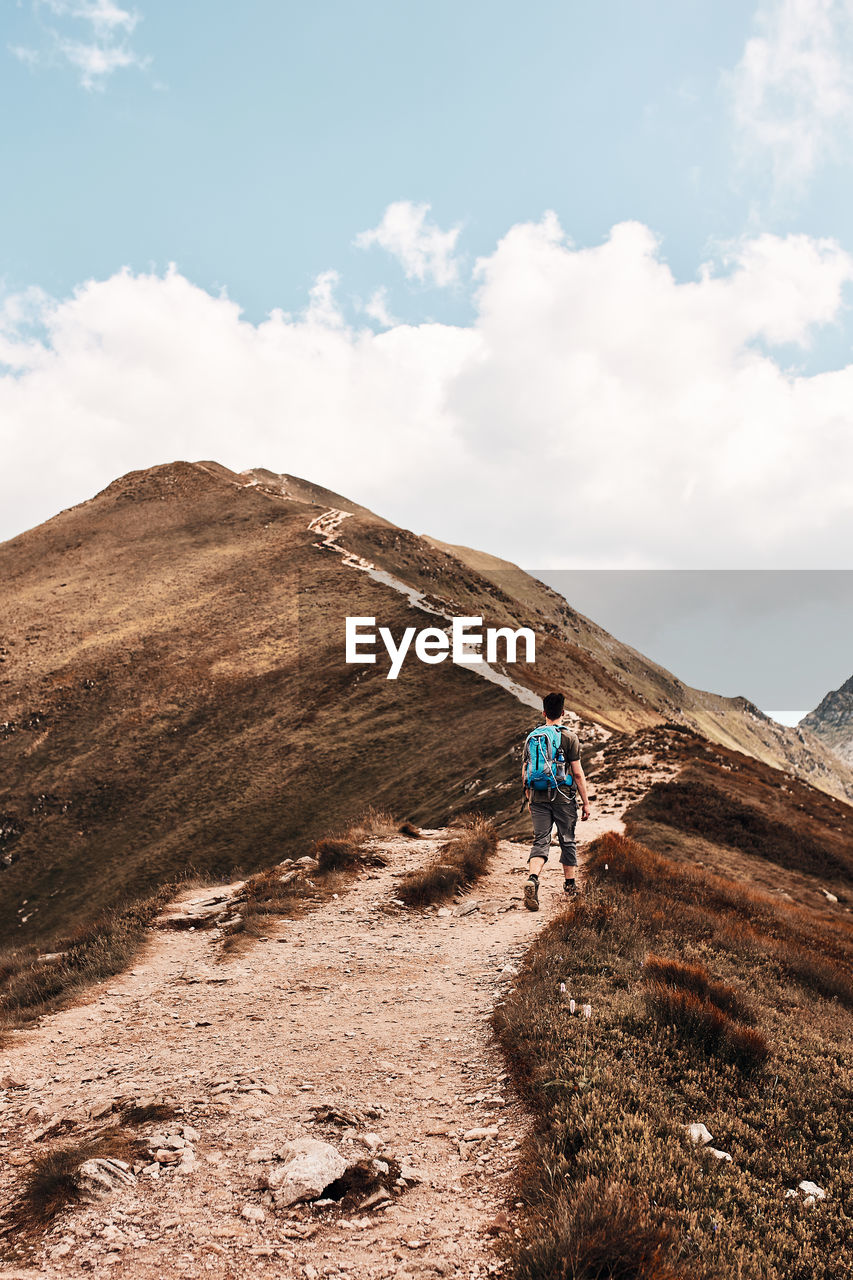 Young man with backpack hiking in a mountains, actively spending summer vacation