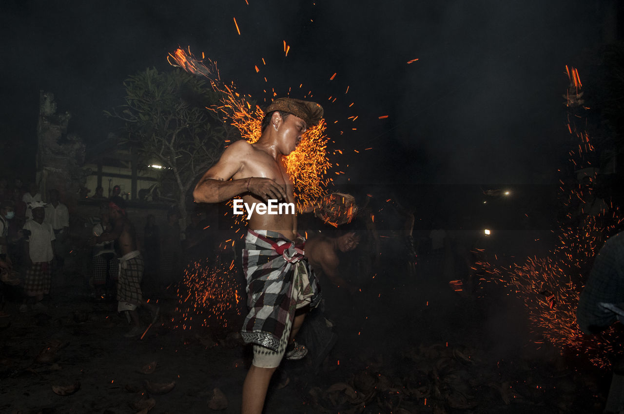 Shirtless man performing stunt with fire at night