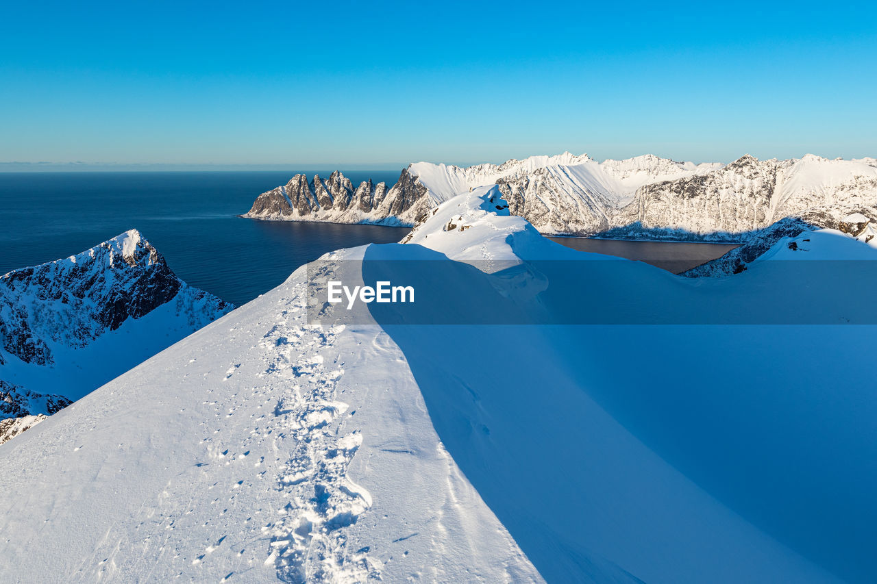 Scenic view of snowcapped mountains by sea against blue sky