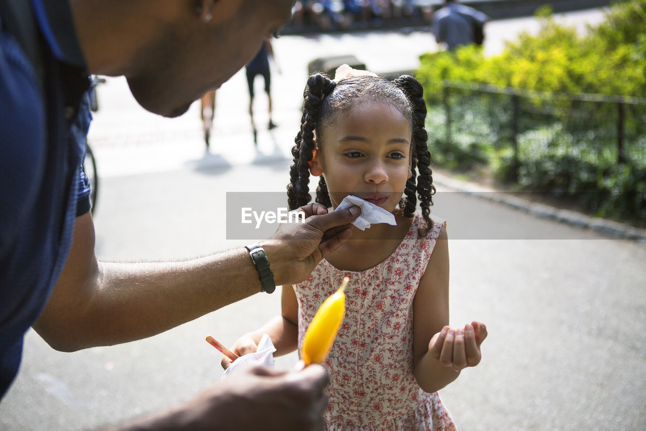 Father cleaning face of daughter with tissue at park