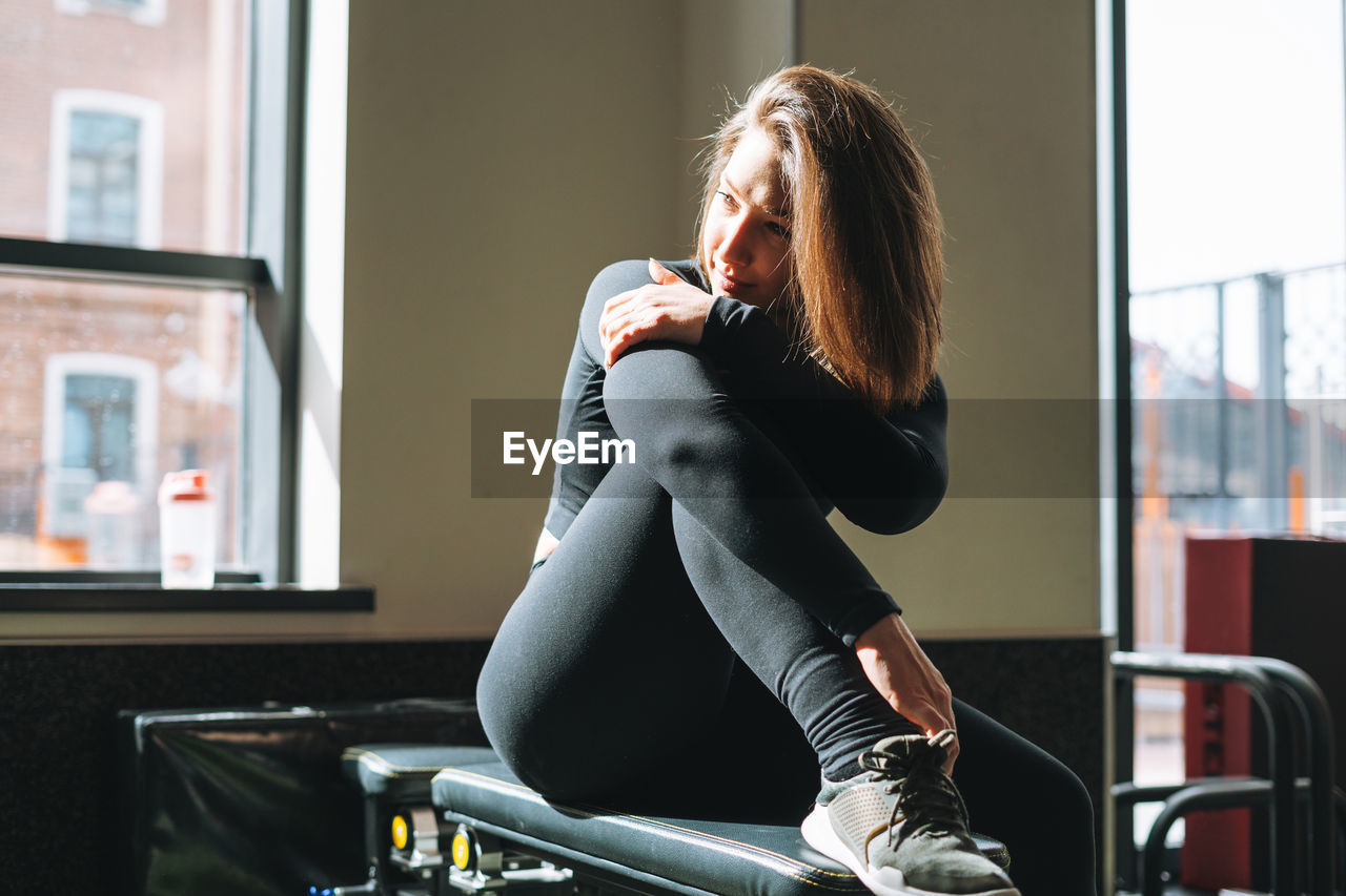 Portrait of resting young brunette woman in sport active wear in the fitness club gym