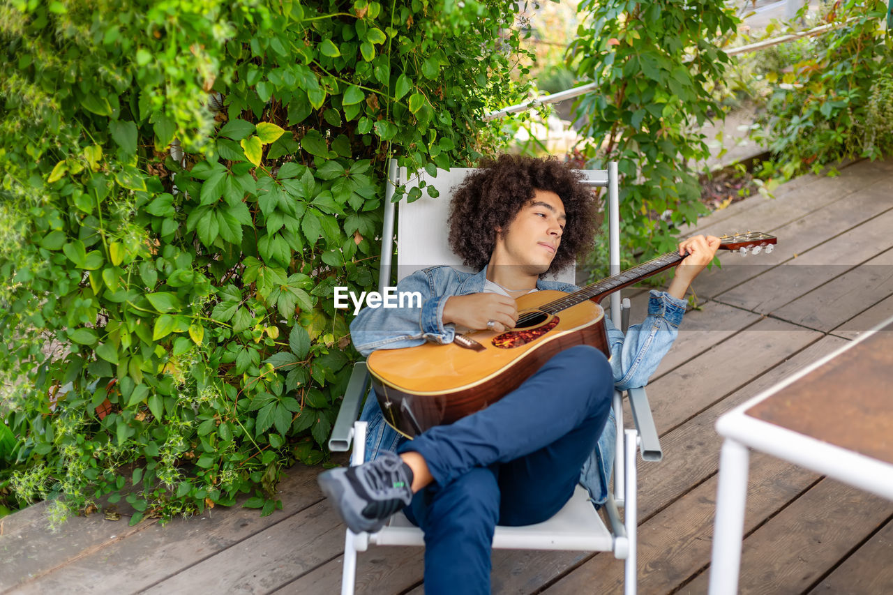 young woman sitting on chair against plants