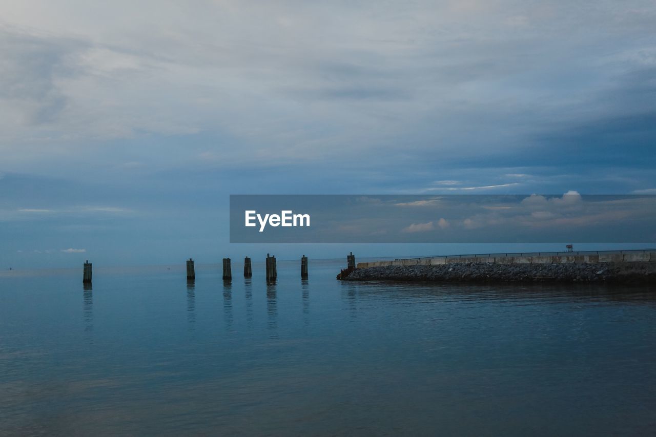 WOODEN POSTS ON SEA AGAINST SKY