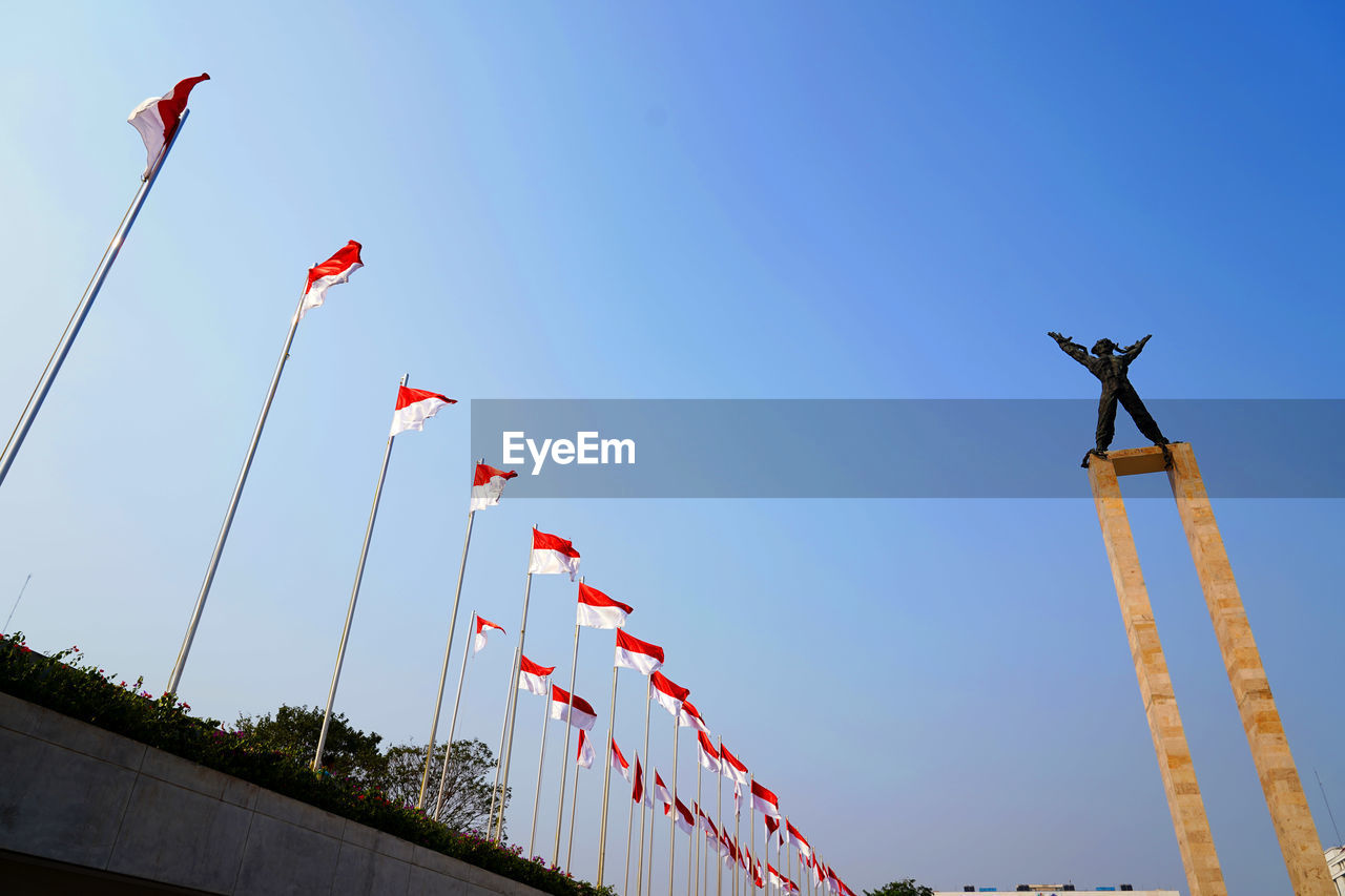 Low angle view of flags against clear blue sky