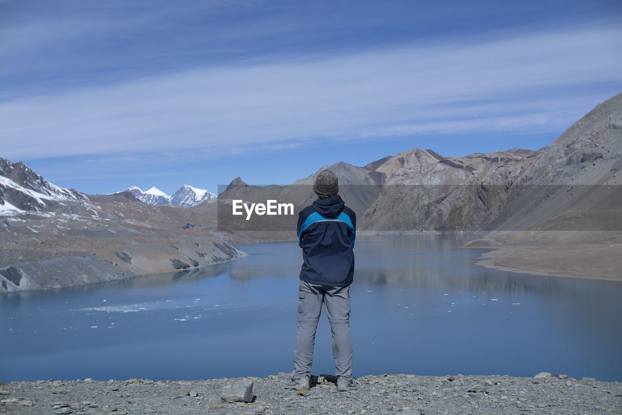 Rear view of man standing on mountain by lake