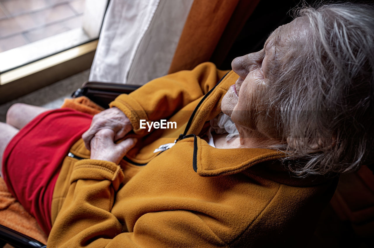 Elderly woman in a wheelchair looking out the window with a sad and suffering look