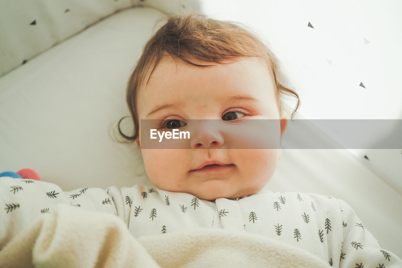 Cute baby girl lying on crib at home