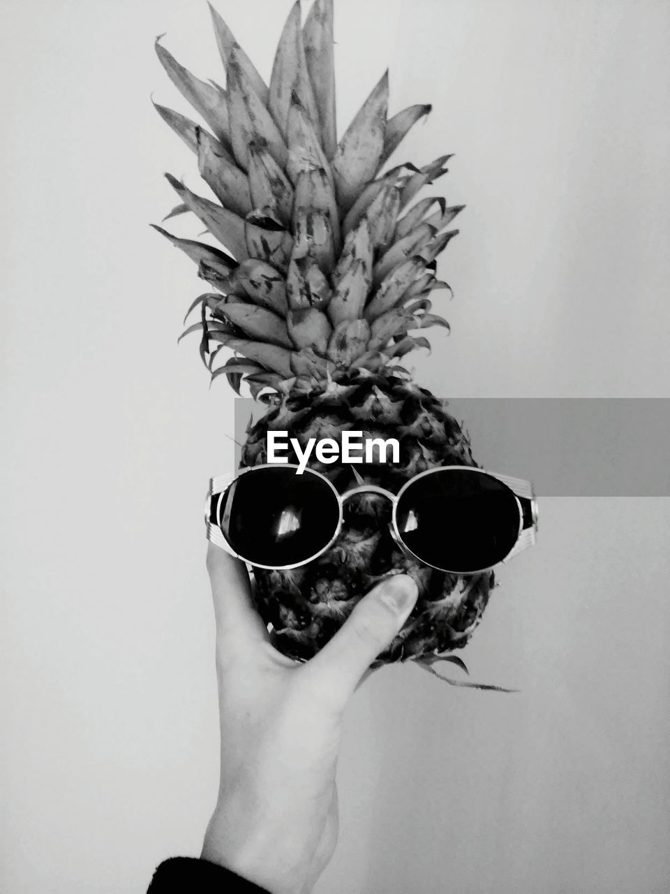 Cropped hand of woman holding pineapple with sunglasses against white background