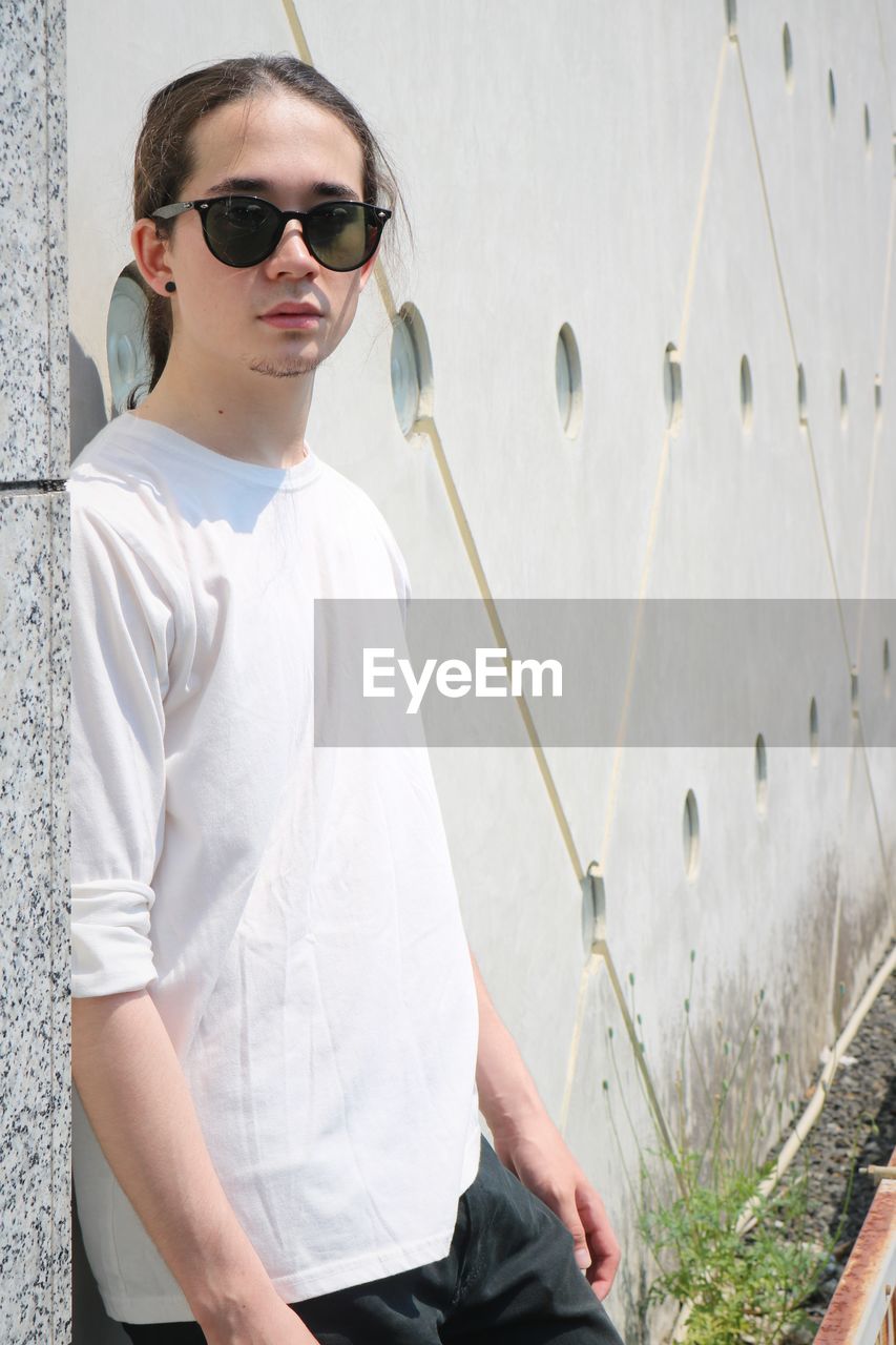 Portrait of young man wearing sunglasses while standing against urban architecture 