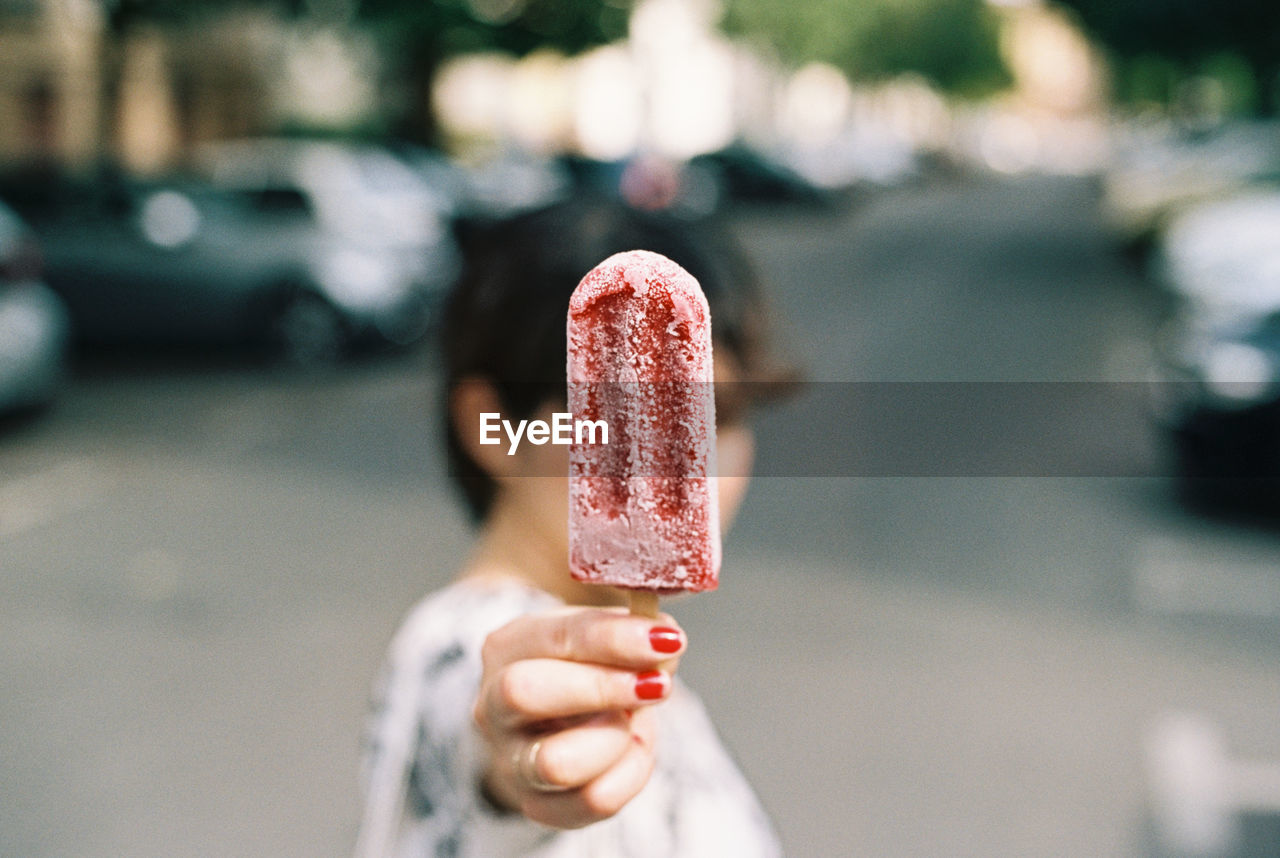 Woman holding flavored ice while standing on street