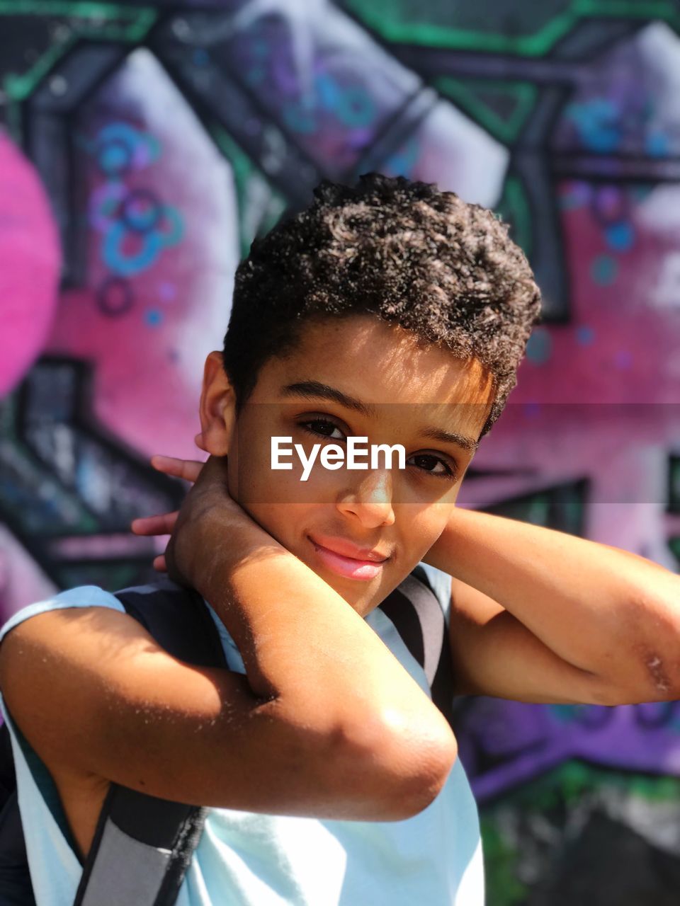 Portrait of cute boy with hands behind head standing against wall